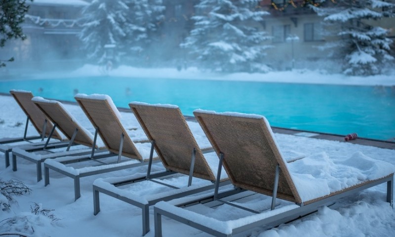 Topli otvoreni bazen sa plavom vodom i ležaljkama prekrivenim snegom po hladnom vremenu