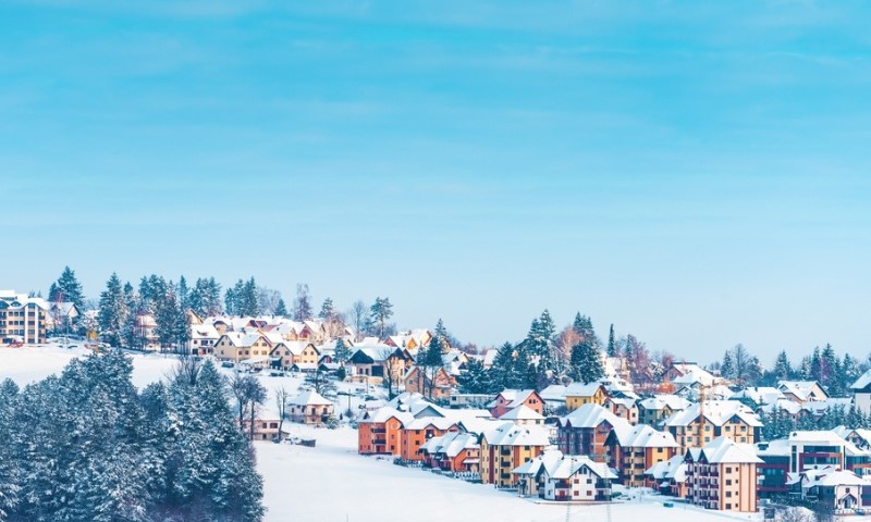 Zlatiborski pejzaž zimi sa šarenim kućama i zimzelenim borovima